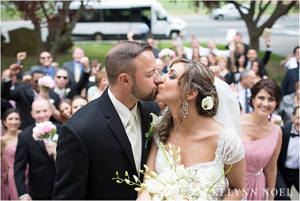 Bride and Groom, Leila and Matt, kissing at the top of the stairs after their wedding ceremony. Their guests are in the background cheering.