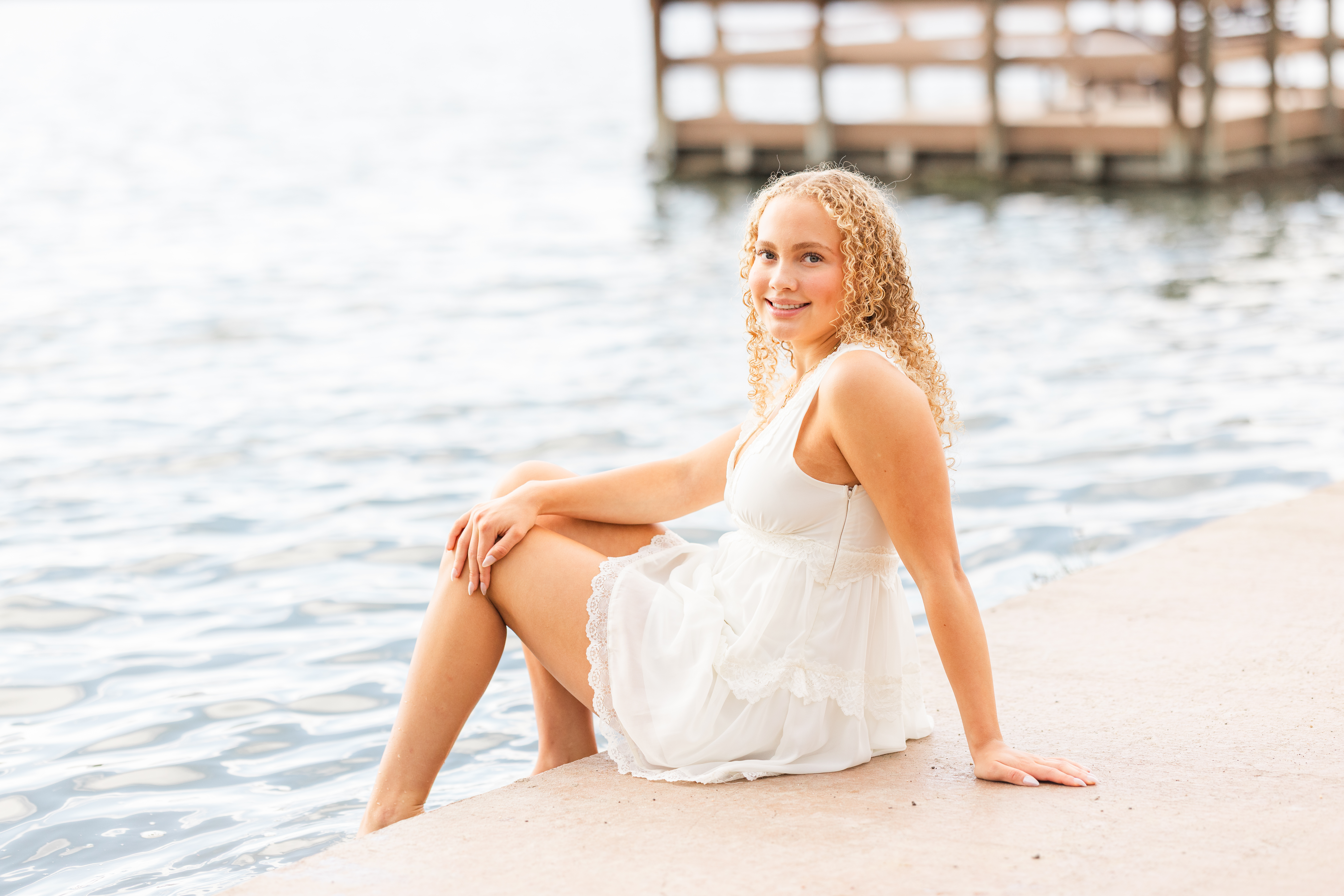A high school senior girl wearing a flowy outfit posing in the tall summer grass at Chautauqua Park with the iconic Flatirons towering in the background under bright sunshine.