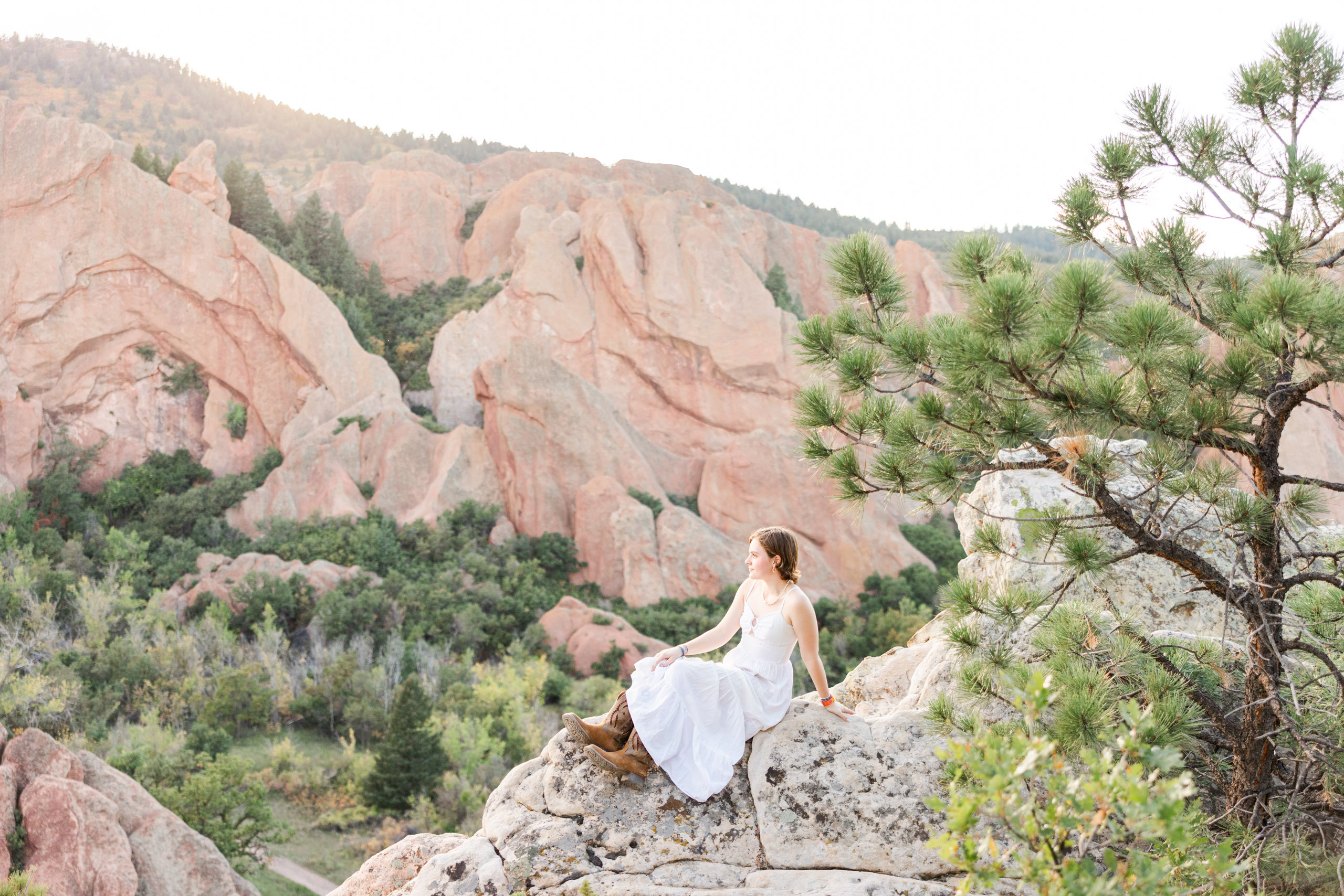A high school senior posing outdoors in Littleton, Colorado, transitioning from lush blooming gardens at Hudson Gardens to towering red rock backdrop vistas at Roxborough State Park.
